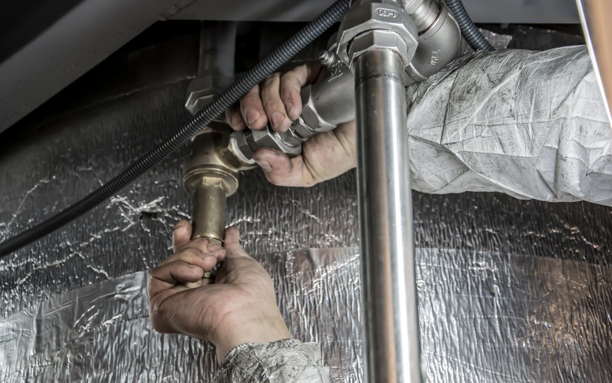 Technician repairing a pipe connection under a sink